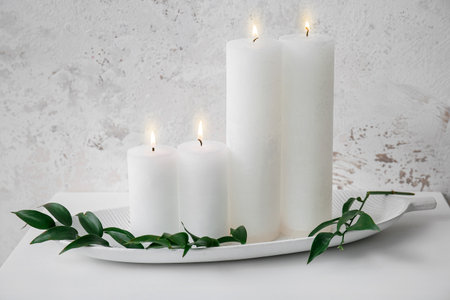 Burning candles and ruscus branch on table near gray grunge wallの写真素材