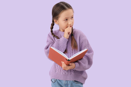 Little girl with book biting nails on lilac backgroundの写真素材