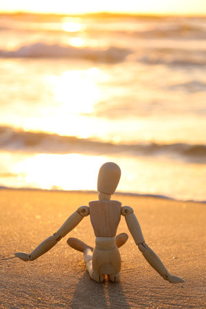 Wooden mannequin on sand near the sea at sunsetの写真素材