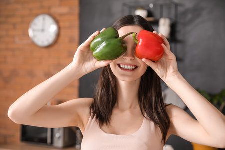 Happy young woman with fresh bell pepper in kitchenの写真素材