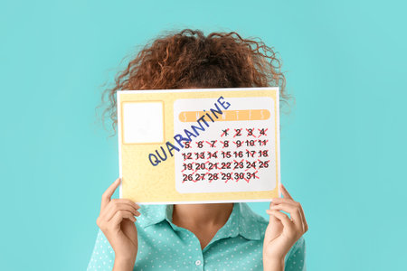 Young woman holding calendar with written word QUARANTINE against color backgroundの写真素材