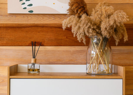 Modern chest of drawers with oil freshener and floral decor near wooden wall in roomの写真素材