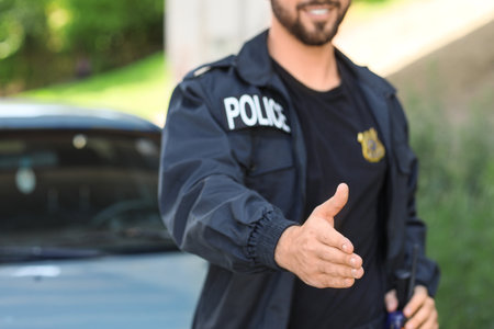 Handsome male police officer giving hand for handshake outdoorsの写真素材
