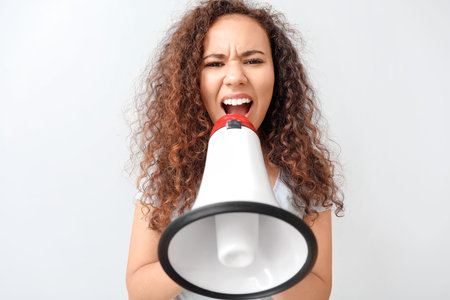 Angry protesting African-American woman with megaphone on light backgroundの写真素材
