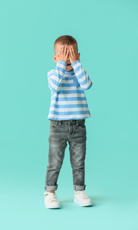 Cute little boy covering his face on color backgroundの写真素材