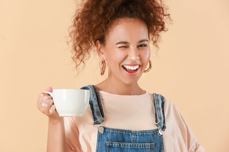 Beautiful young African-American woman with hot tea on color backgroundの写真素材