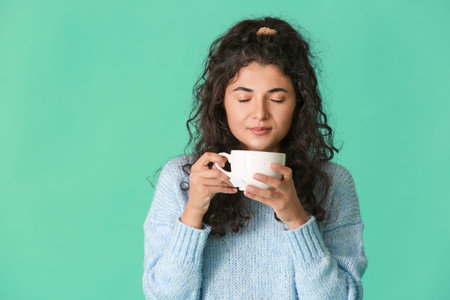 Beautiful young woman with hot tea on color background
