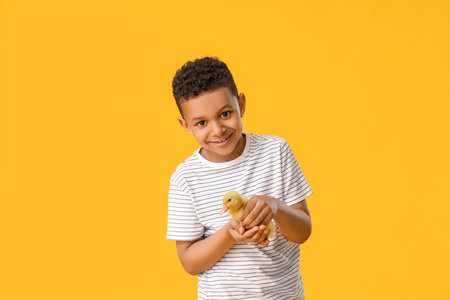 Little African-American boy with cute duckling on color background