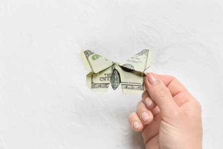 Female hand with origami butterfly made of dollar banknote on white backgroundの写真素材