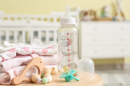 Bottle for baby with pacifier, toy and clothes on table in room