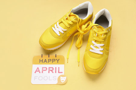Paper with text HAPPY APRIL FOOLS and sneakers on yellow backgroundの写真素材