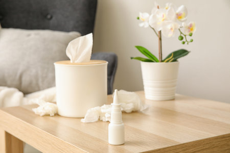 Nasal drops with tissue box on table in living room, closeup. Allergy concept