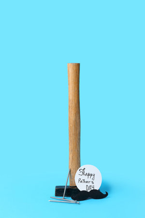 Paper with text HAPPY FATHER'S DAY, hammer, nails and mustache on blue background