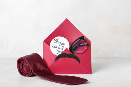 Envelope with text HAPPY FATHER'S DAY, eyeglasses, paper mustache and necktie on white background