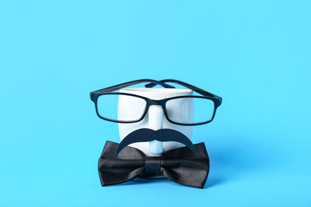 Cup with paper mustache, eyeglasses and bow tie on blue background. father's day celebrationの写真素材
