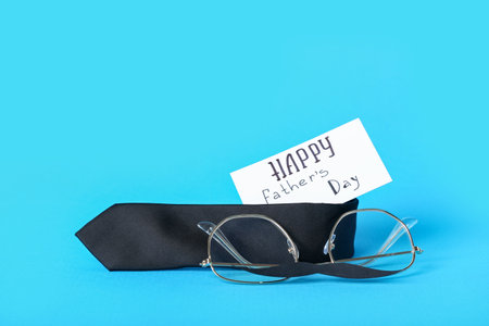 Paper with text HAPPY FATHER'S DAY, necktie and eyeglasses on blue backgroundの写真素材