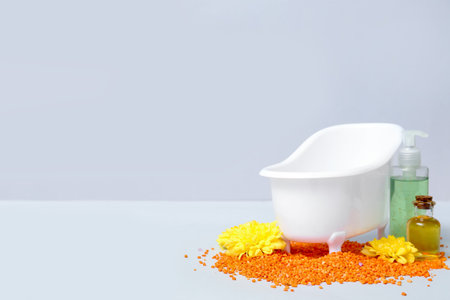 Small bathtub, bottles of cosmetic products, flowers and sea salt on light backgroundの写真素材