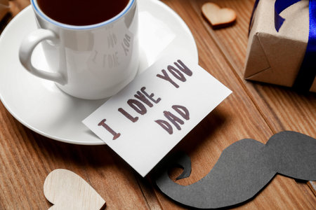 Cup of coffee, paper mustache and card with text I LOVE YOU DAD on wooden table, closeup. father's...