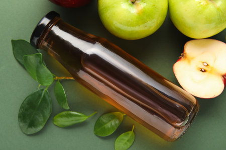 Glass bottle of fresh apple cider vinegar and fruits on green backgroundの写真素材