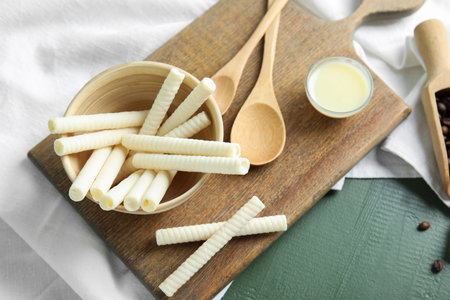 Board with delicious wafer rolls, condensed milk and spoons on green wooden backgroundの写真素材