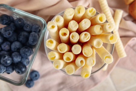 Glass of delicious wafer rolls and bowl with blueberries on pink napkin, closeupの写真素材
