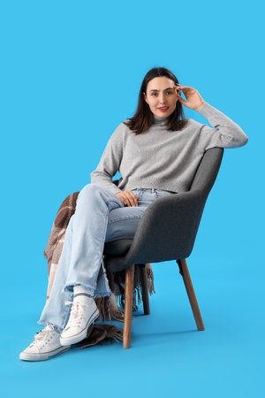 Young woman sitting in black armchair on blue backgroundの写真素材