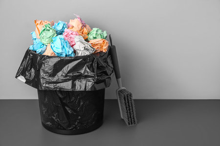 Rubbish bin with crumpled paper and brush near gray wall