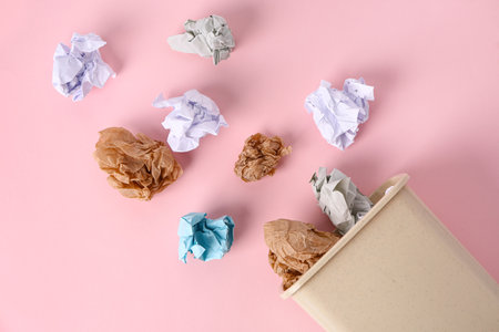 Rubbish bin with crumpled paper on pink backgroundの写真素材