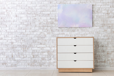 Modern chest of drawers near brick wall in roomの写真素材