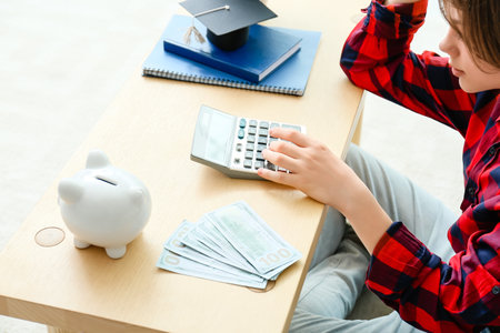 Teenage boy with savings for education and calculator at homeの写真素材