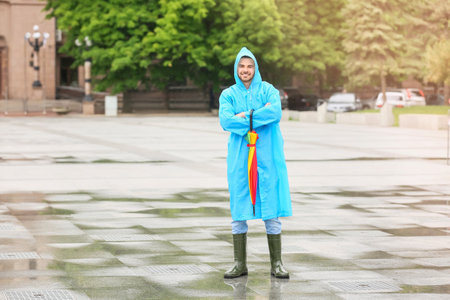 Young man with umbrella wearing raincoat outdoorsの写真素材