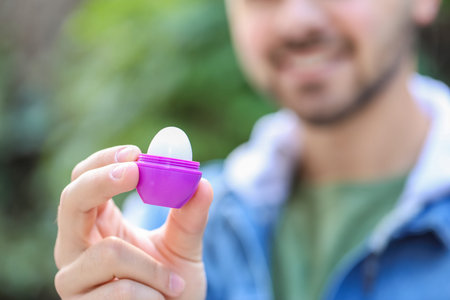 Handsome young man with lip balm outdoors, closeup