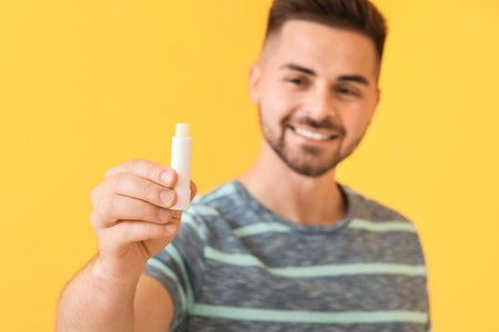 Handsome young man with lip balm on color backgroundの写真素材