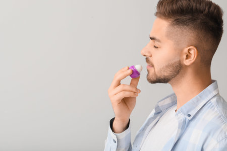 Handsome young man with lip balm on light background