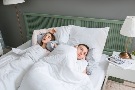 Young irritated man in bed with snoring wifeの写真素材