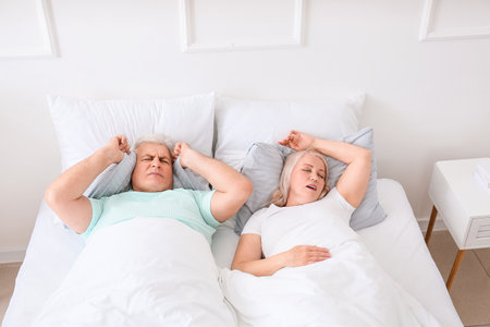 Mature irritated man in bed with snoring wifeの写真素材