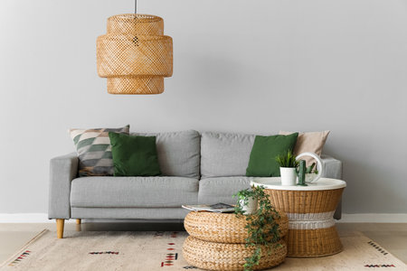 Cozy sofa with cushions, houseplants, table and wicker pouf near gray wallの写真素材