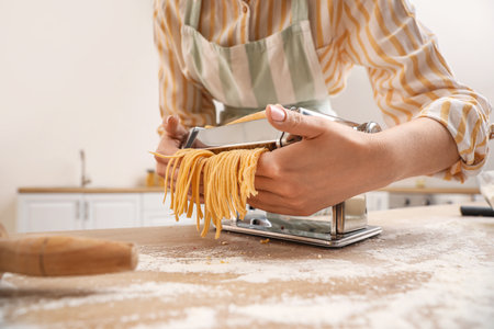 Woman making pasta with machine at table in kitchen, closeupの写真素材