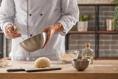 Male chef making dough for pasta at table in kitchen, closeupの写真素材