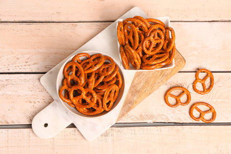 Board with bowls of tasty pretzels on light wooden backgroundの写真素材