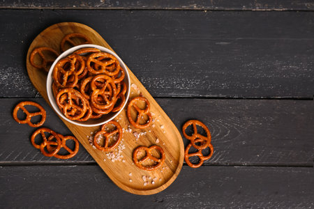 Board with bowl of tasty salted pretzels on dark wooden backgroundの写真素材