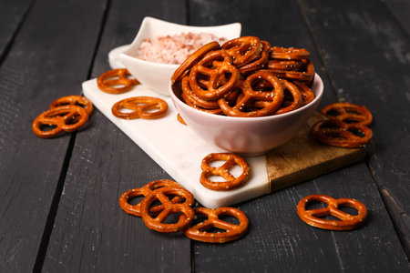 Board with bowls of tasty pretzels and sea salt on dark wooden backgroundの写真素材