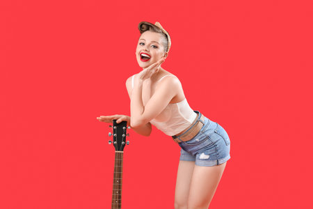 Surprised young pin-up woman with guitar on red backgroundの写真素材