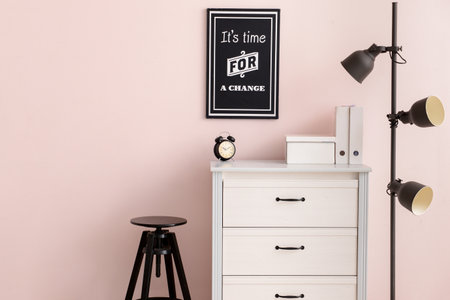 Modern chest of drawers with lamp and stool near color wall in officeの写真素材