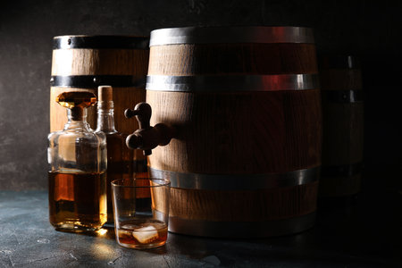 Wooden barrels, bottles and glass of cold whiskey on dark backgroundの写真素材