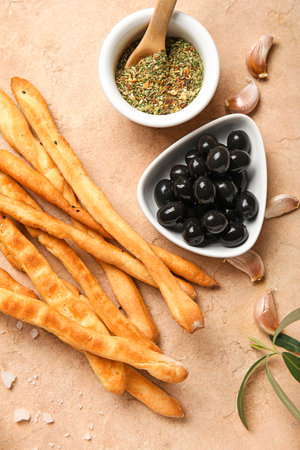 Tasty Italian Grissini with bowls of herbs and black olives on beige backgroundの写真素材