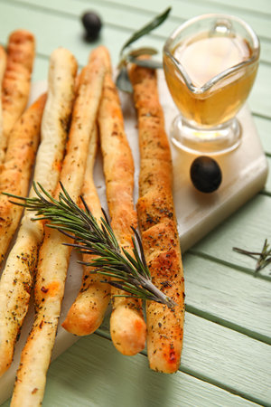 Board with tasty Italian Grissini on green wooden background, closeup