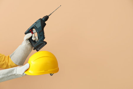 Female builder with hardhat and drill on beige backgroundの写真素材