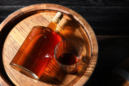 Oak barrel with glass and bottle of tasty whiskey on dark wooden backgroundの写真素材