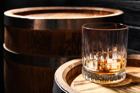 Glass of cold whiskey and oak barrels on dark wooden backgroundの写真素材